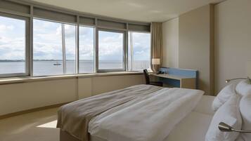 A hotel room with a large window offering a view of the sea and a ship. The room has a bed, a desk, and a chair.