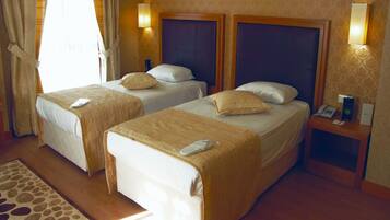 A hotel room with two single beds, a bedside table with a phone and a book, and a small desk with a lamp.