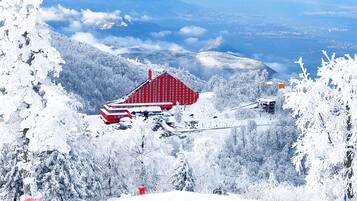 A snow-covered mountain landscape with a red building featuring a steep roof, surrounded by snow-laden trees and a clear sky.