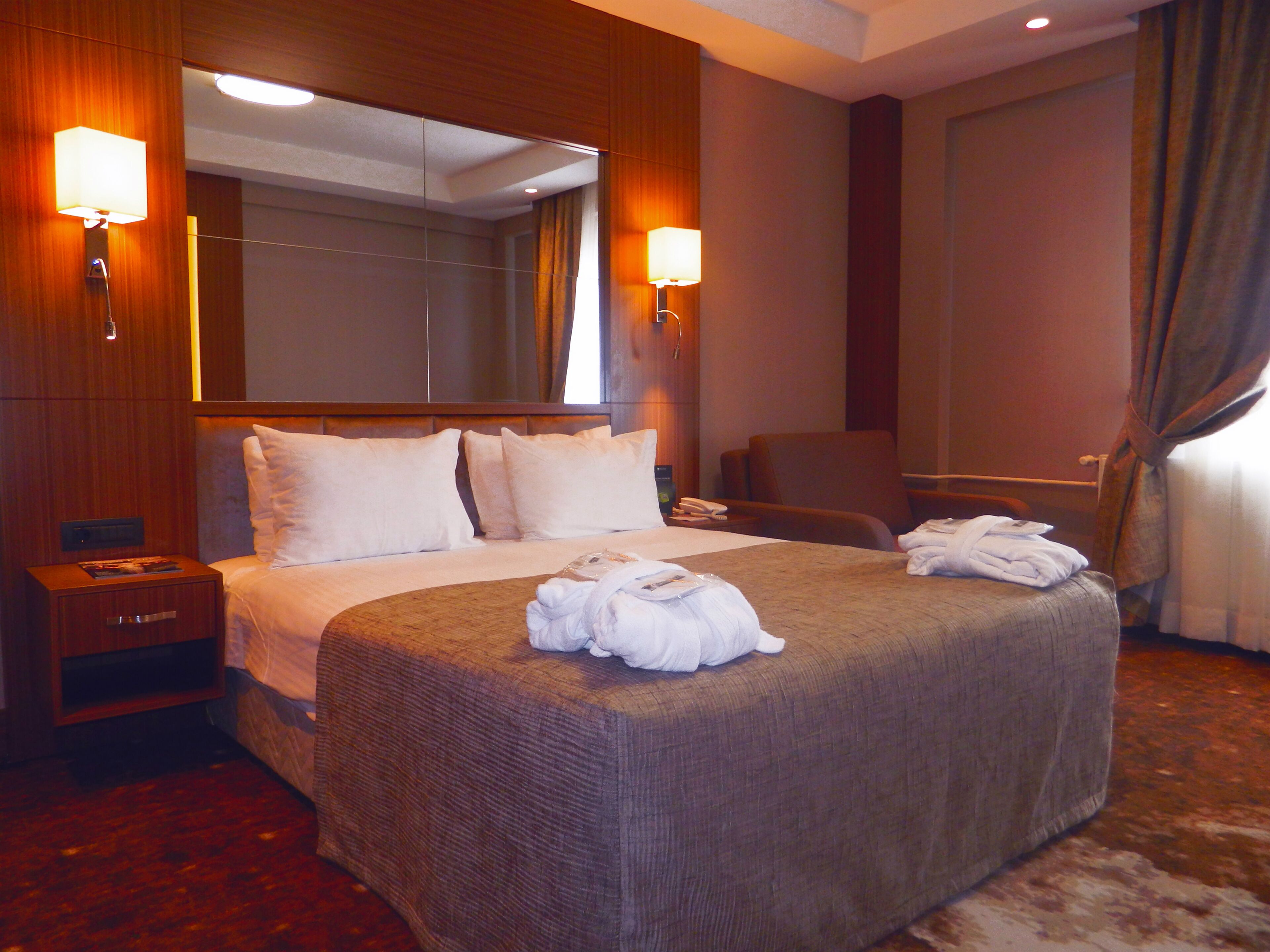 Una habitación de hotel con una cama grande, dos mesitas de noche, una silla, un escritorio y un espejo.