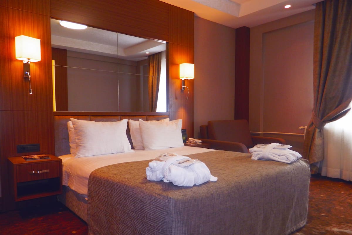 A hotel room with a large bed, two bedside tables, a chair, a desk, and a mirror.