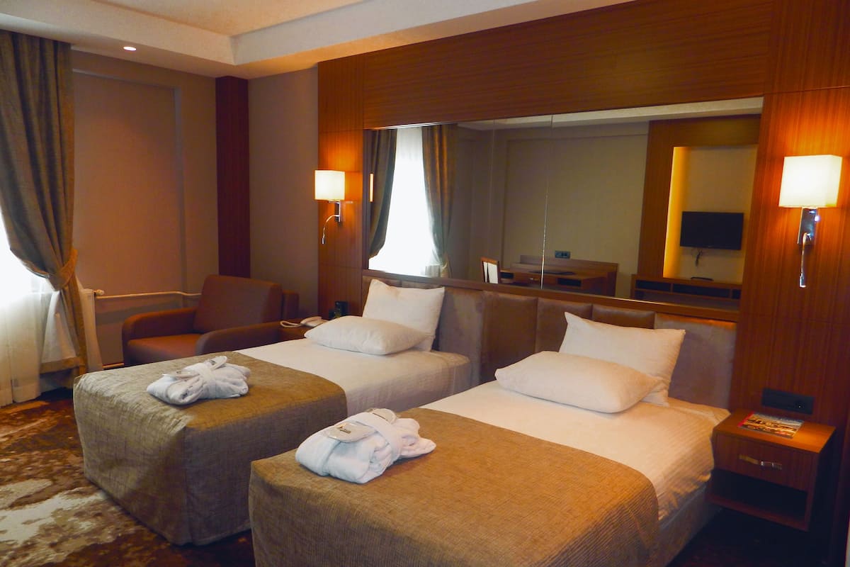 A hotel room with two beds, a chair, a desk, and a TV.