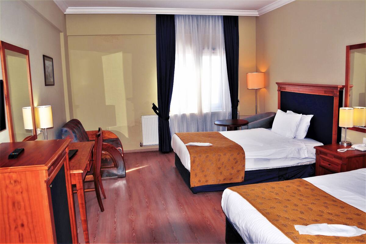 A hotel room with two beds, a desk, a chair, a lamp, and a window with curtains.