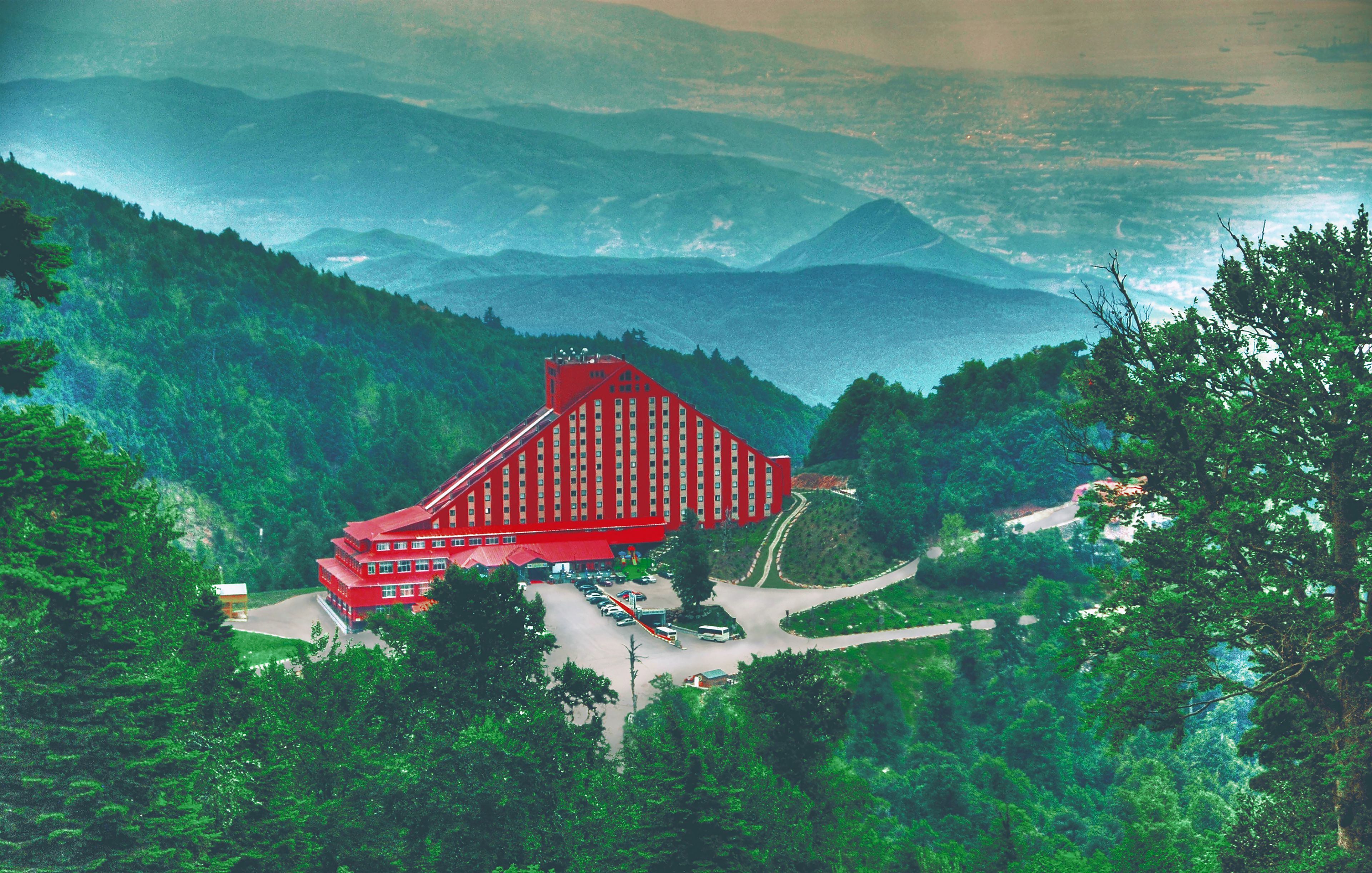 A red building with a unique architectural design, surrounded by lush green hills and a mountainous backdrop.