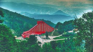 A red building with a unique architectural design, surrounded by lush green hills and a mountainous backdrop.