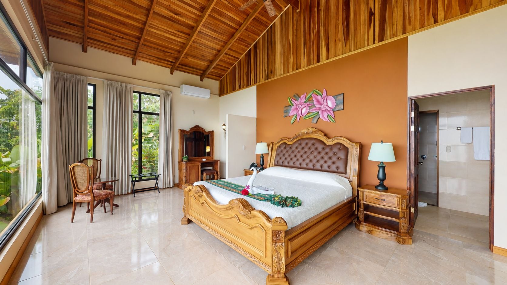 A spacious bedroom with a large bed, a wooden headboard, and a view of greenery through the window.