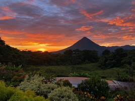 Un paisaje montañoso con atardecer, vegetación exuberante y una masa de agua.