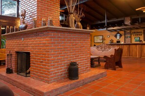 A brick fireplace with a mantel, a wooden bench, and a table with a vase. - Hotel Arenal Lodge (La Fortuna)
