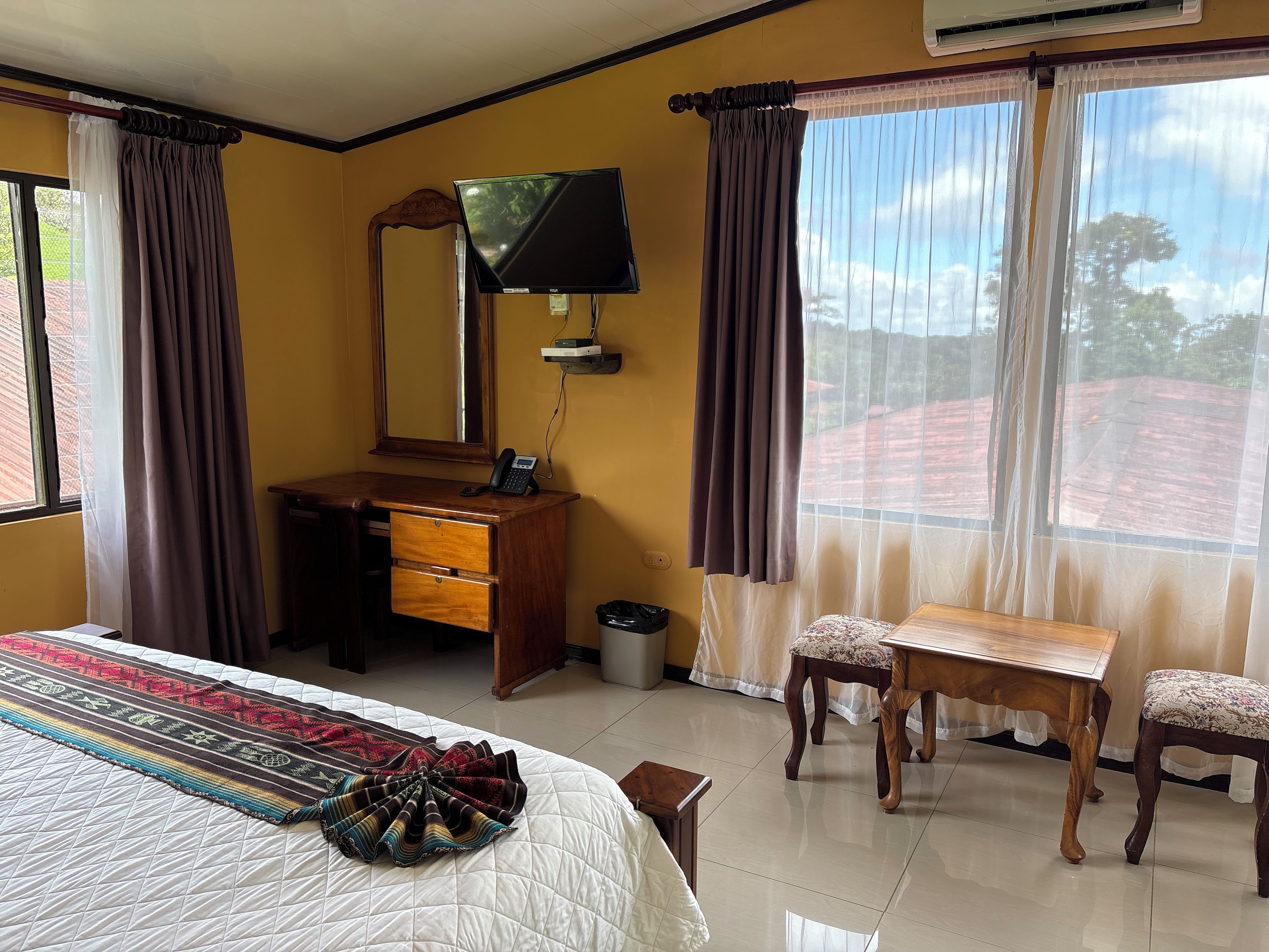 A hotel room with a bed, a desk with a telephone, a chair, a table, and a television.