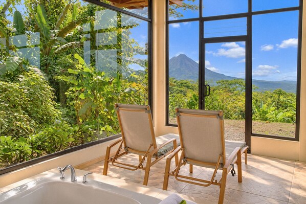 Una habitación con un ventanal grande, dos sillas de madera, una bañera y vistas a una montaña.