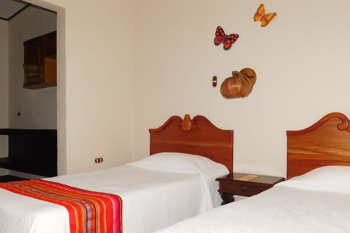 A hotel room with two single beds, a wooden headboard, a nightstand, and a wall-mounted lamp.