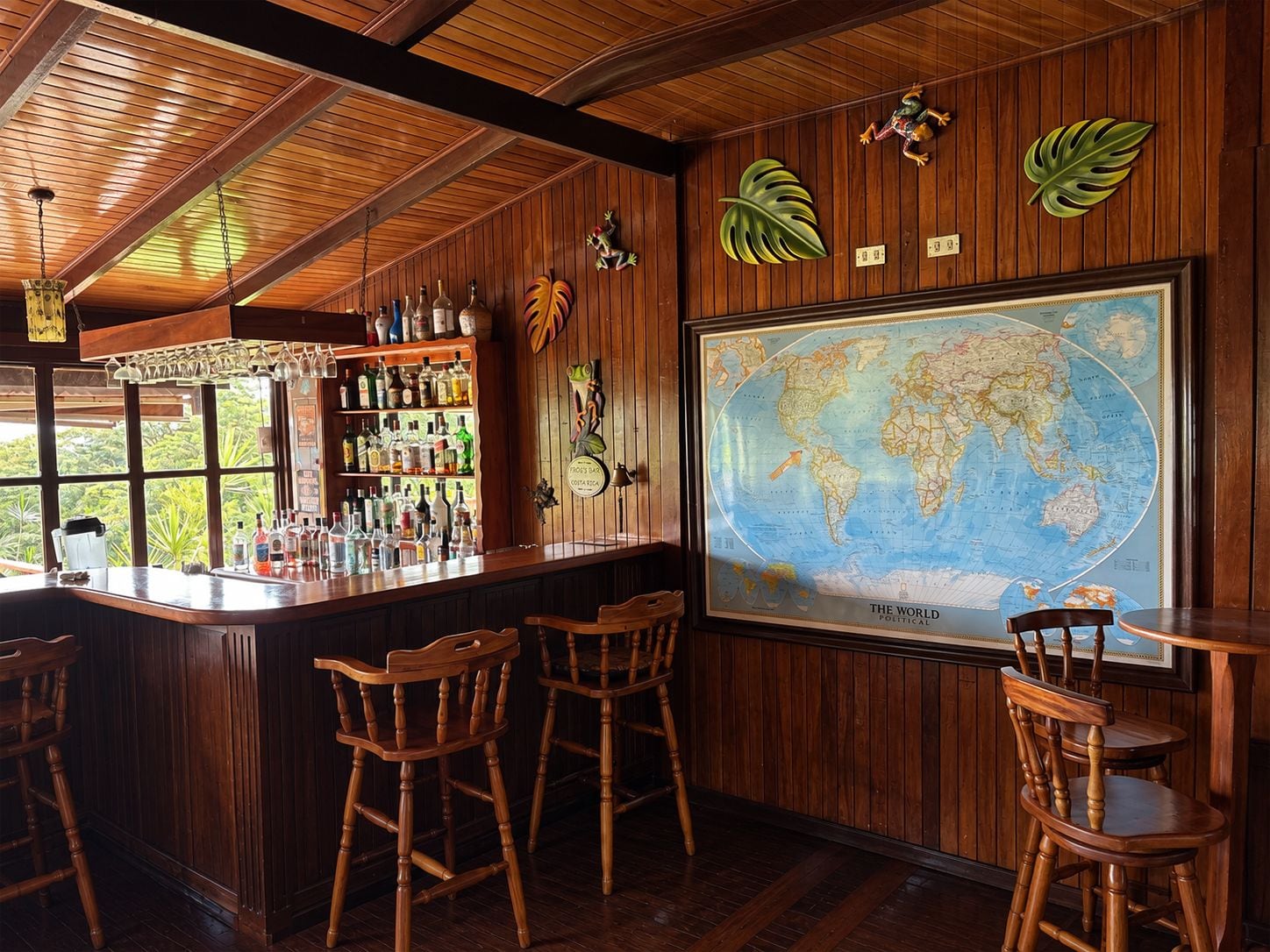 A bar area with wooden furniture, a large world map, and tropical leaf decorations.
