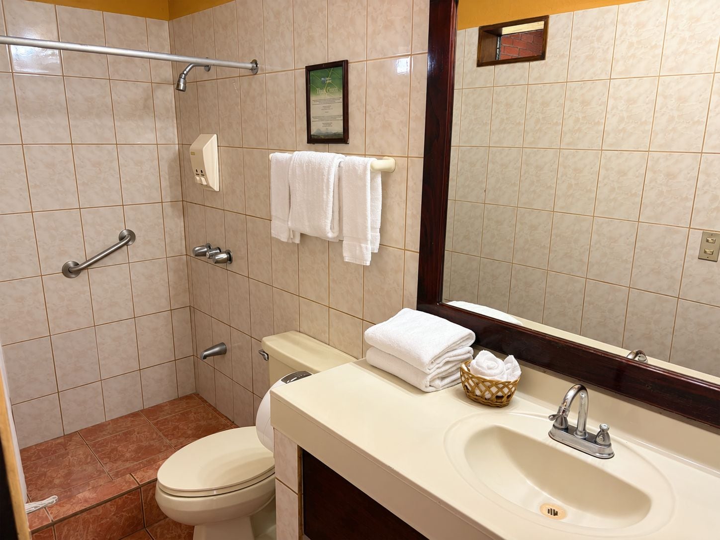 Un baño con inodoro, lavabo y ducha. Hay toallas y un certificado enmarcado en la pared.