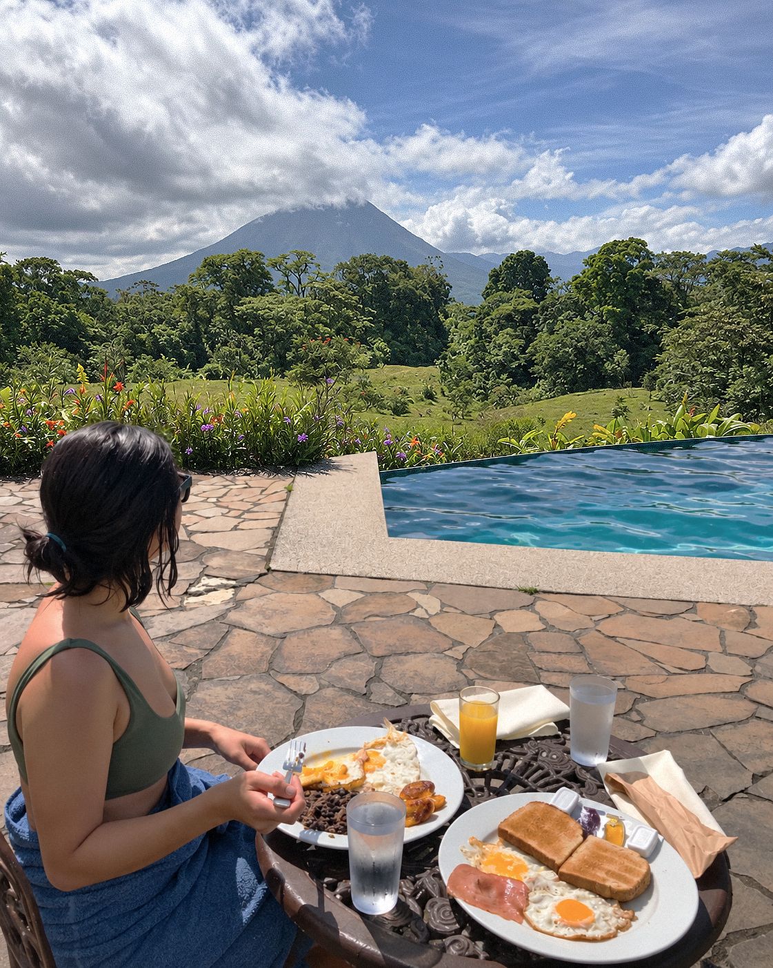 Una persona cenando al aire libre con vistas a la montaña, una piscina y un patio de piedra.
