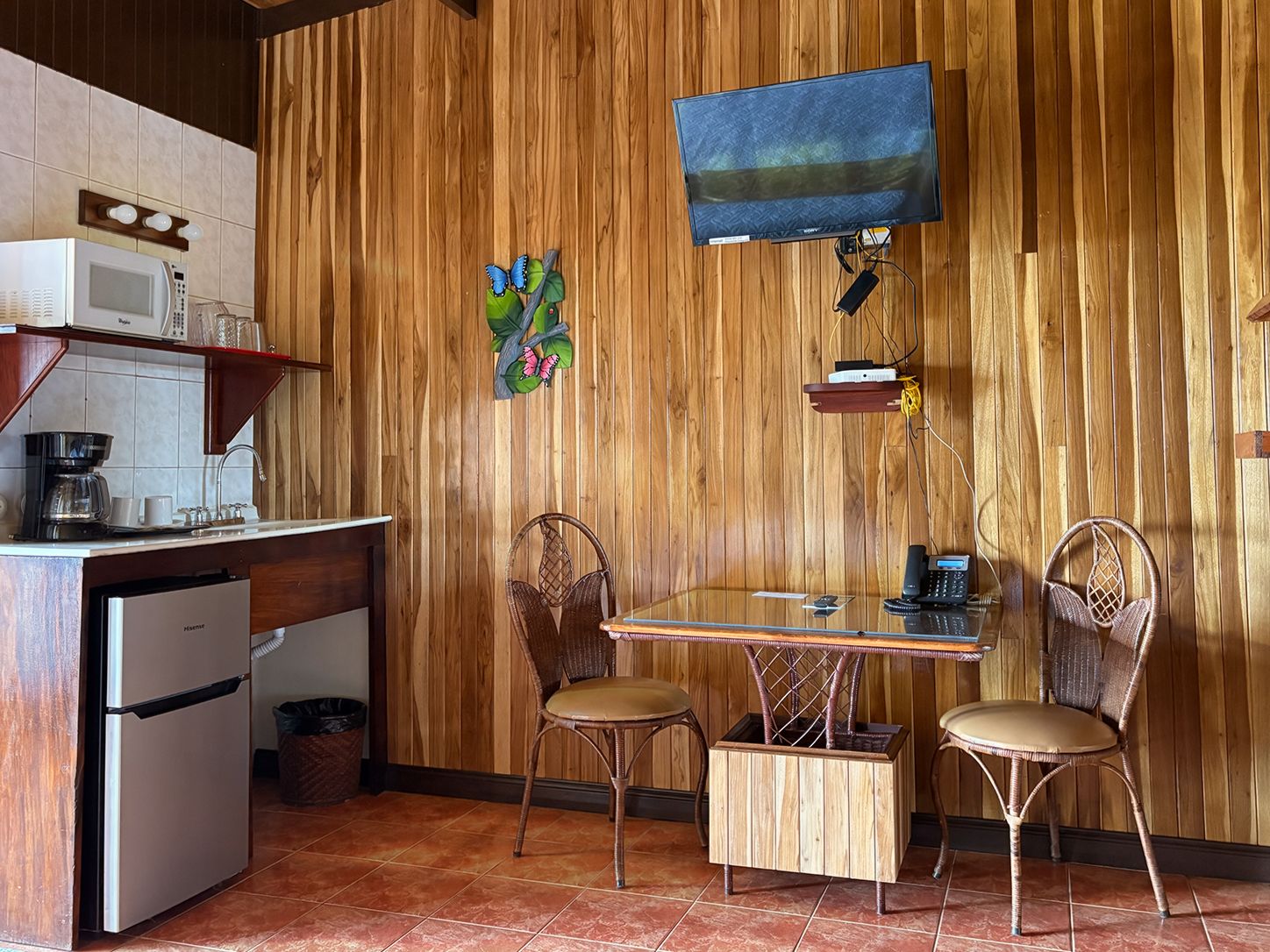 Een keuken met een houten wand, een televisie boven een tafel met stoelen en een magnetron op het aanrecht.