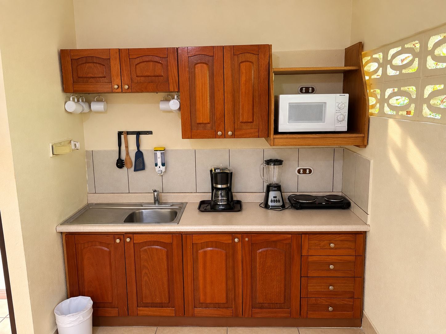 Cozinha compacta com armários de madeira, micro-ondas, máquina de café e liquidificador.