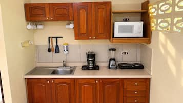 Cozinha compacta com armários de madeira, micro-ondas, máquina de café e liquidificador.