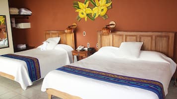 A hotel room with two beds, a wooden headboard, a nightstand with a phone, and a wall-mounted lamp.