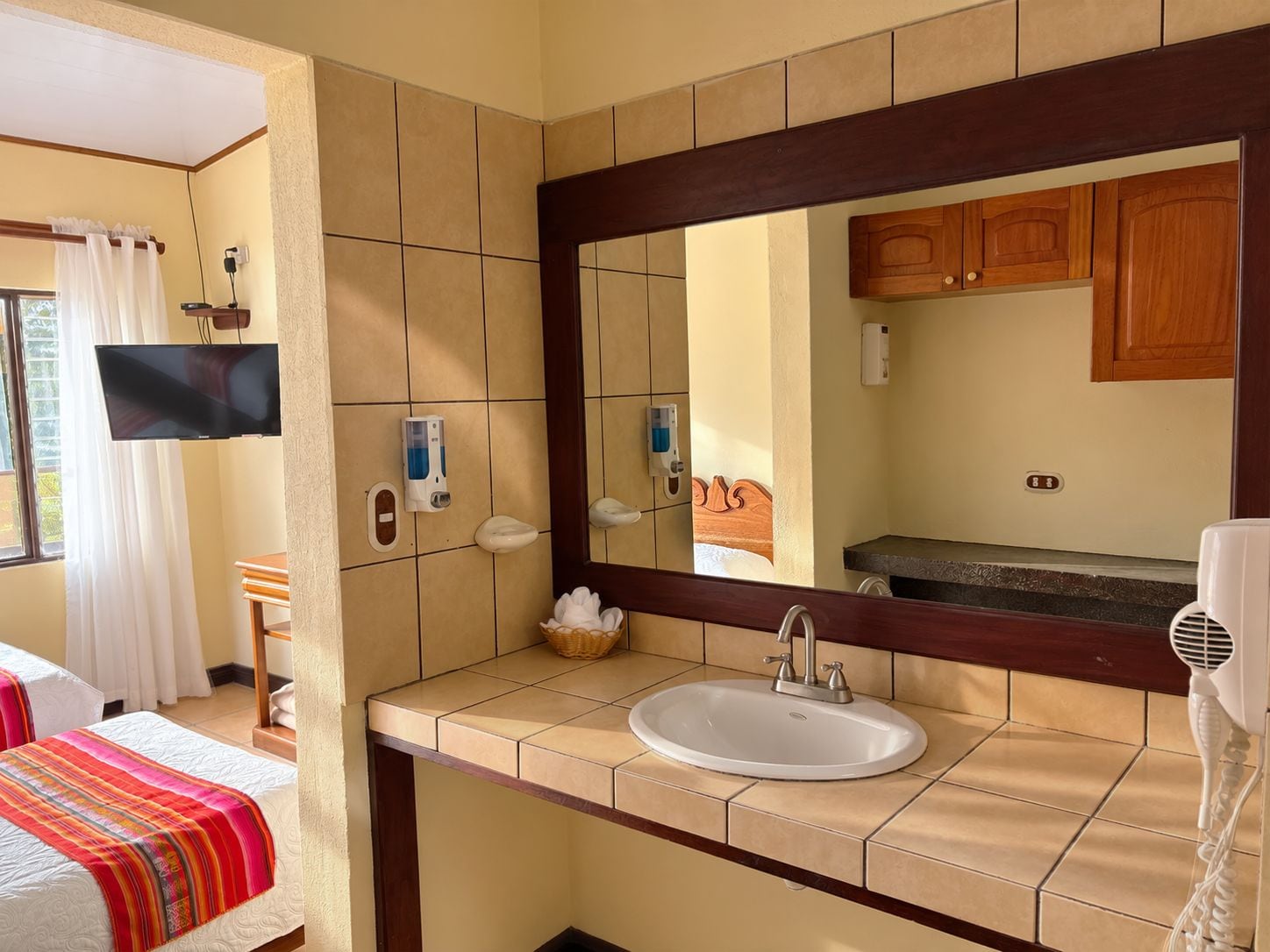 Un baño de hotel con un espejo grande, un lavamanos y un televisor montado en la pared.