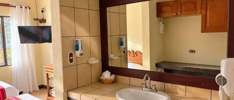 Un baño de hotel con un espejo grande, un lavamanos y un televisor montado en la pared.