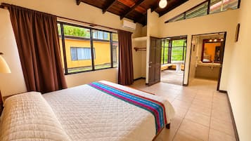 A hotel room with a large bed, a window with curtains, a bathroom with a sink and mirror, and a view of the outside.
