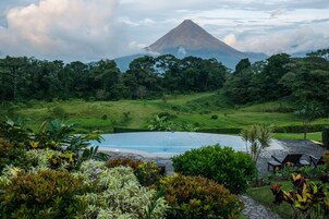 Piscina rodeada por vegetação exuberante e uma montanha ao fundo.