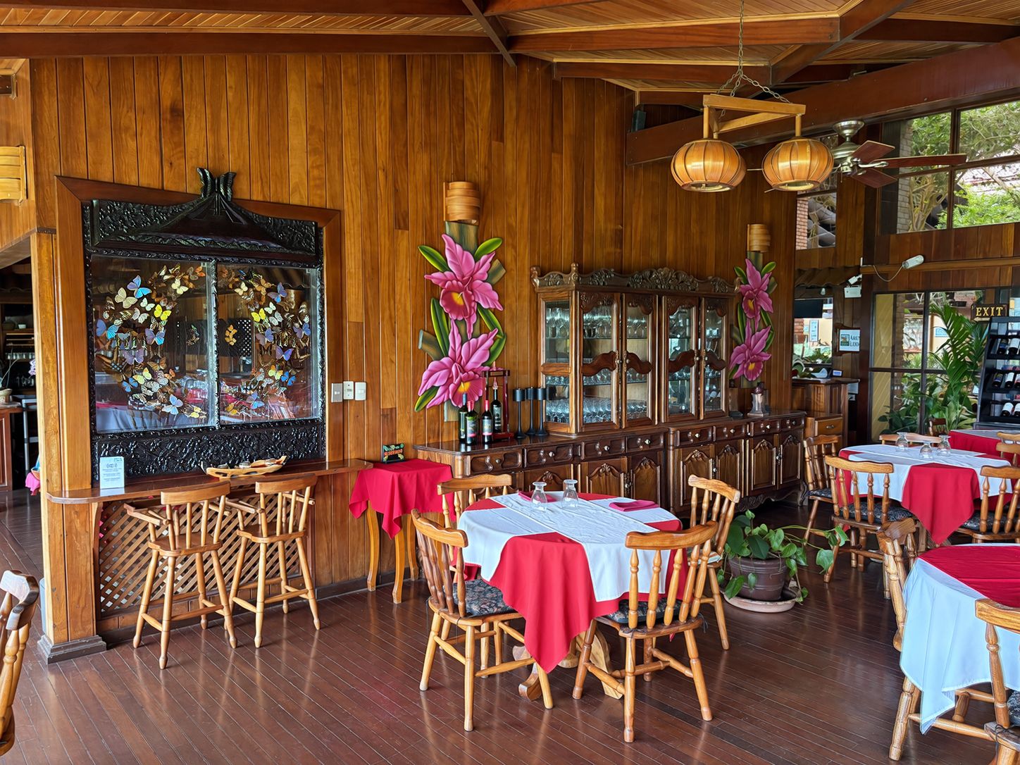 Een restaurant met houten lambrisering, meerdere tafels met rode tafelkleden en een groot raam met uitzicht.