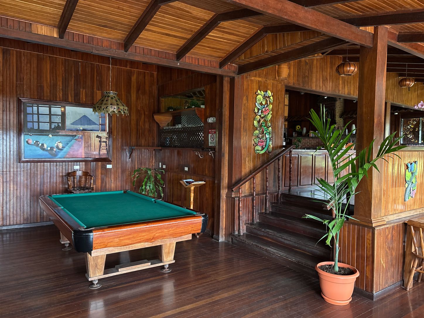 Un interior de madera con mesa de billar, escalera y zona de bar.