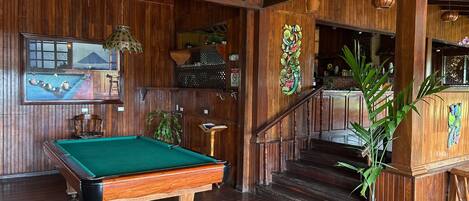 Un interior de madera con mesa de billar, escalera y zona de bar.