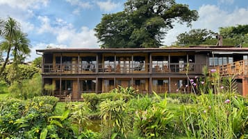 A two-story building with balconies, surrounded by lush greenery and a pond.