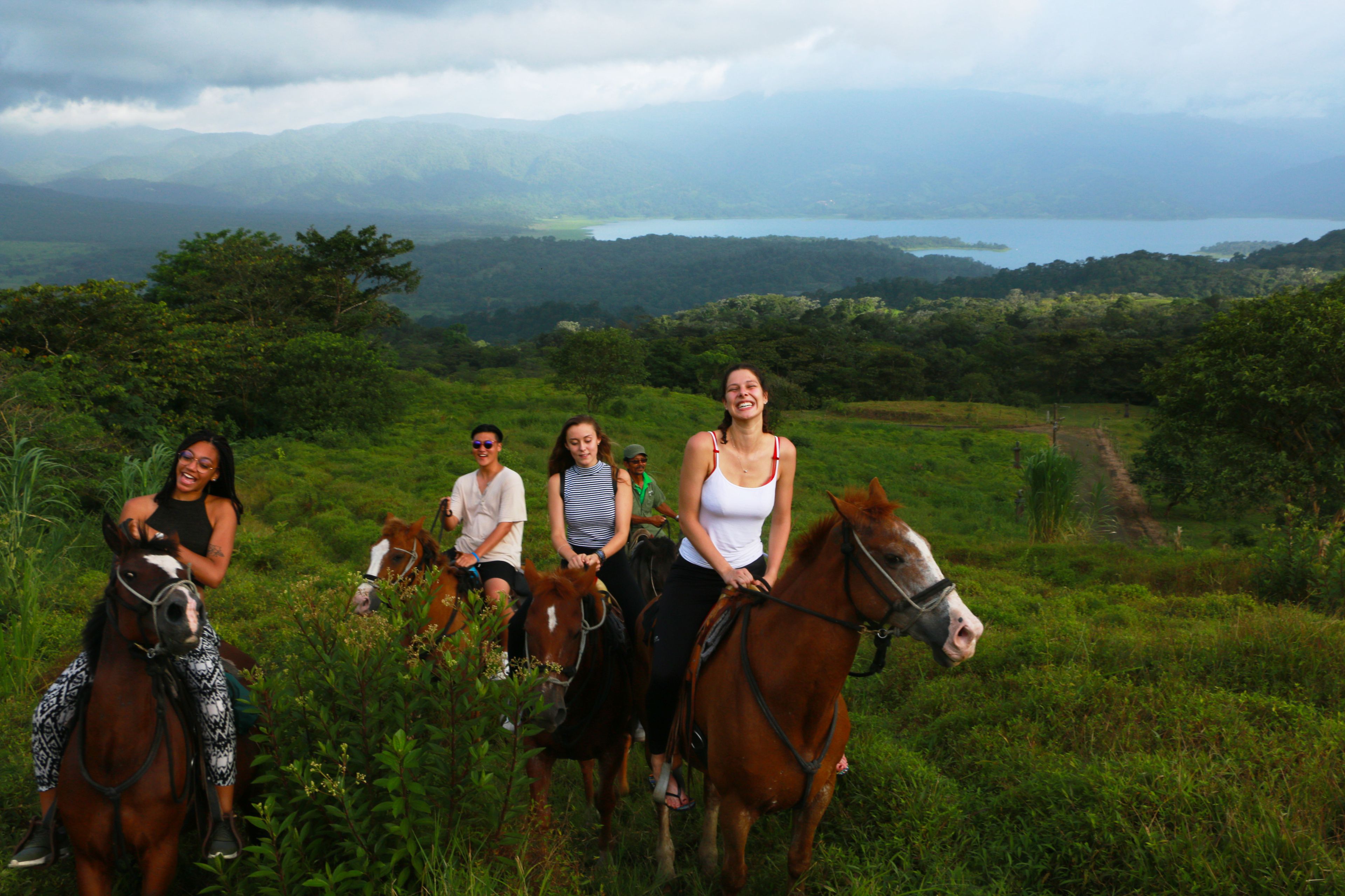 A group of people on horseback in a grassy field with mountains in the background.