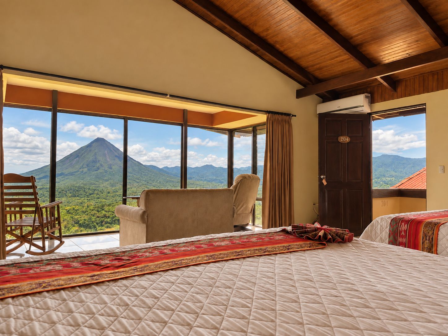 Une chambre d’hôtel avec un lit, une chaise, une grande fenêtre donnant sur la montagne et une porte portant un numéro.