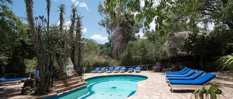 Una piscina con sillas reclinables azules y escalones de piedra.