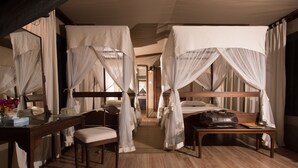 A room with a wooden floor, a desk with a chair, a bedside table with a handbag, and a bed with white curtains.