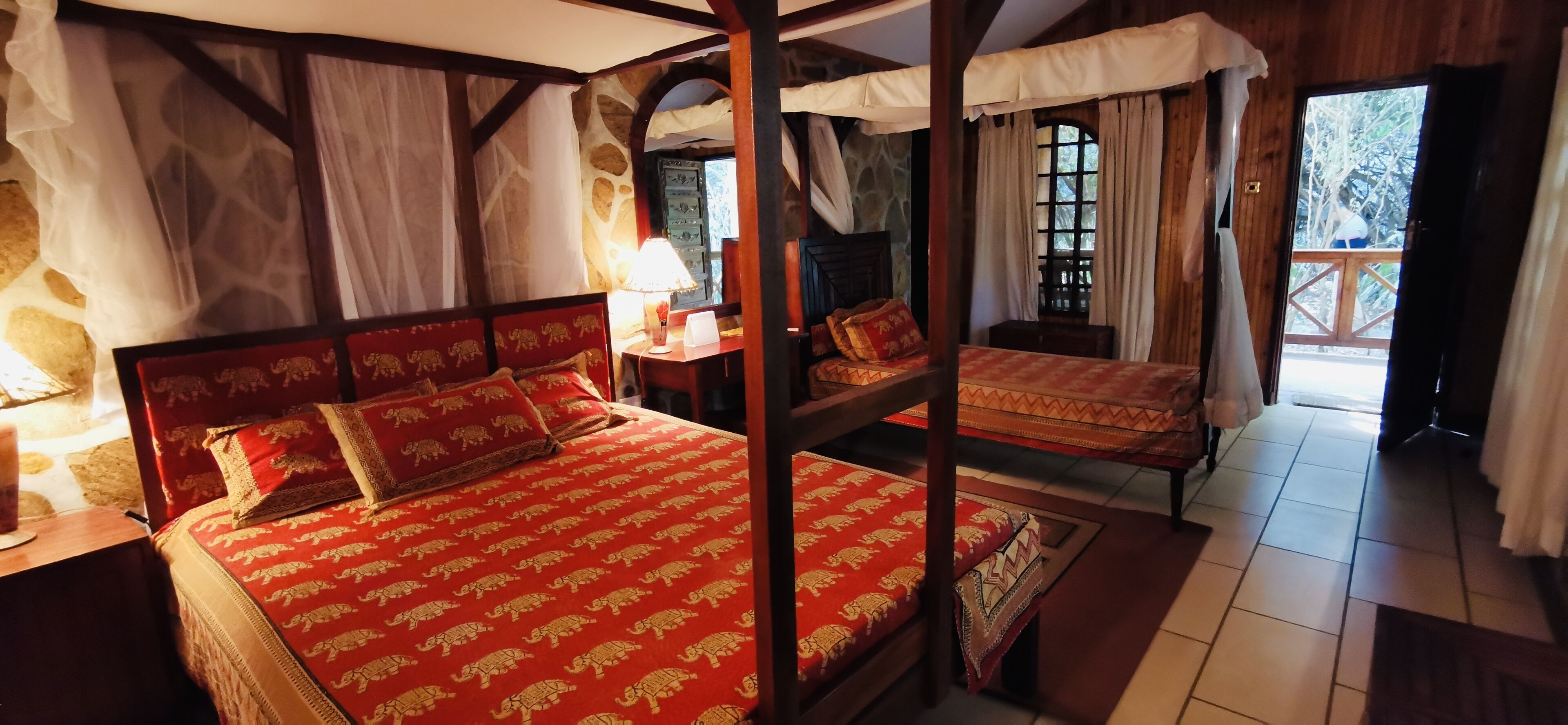 A room with a large bed, a nightstand, a lamp, and a window with curtains.