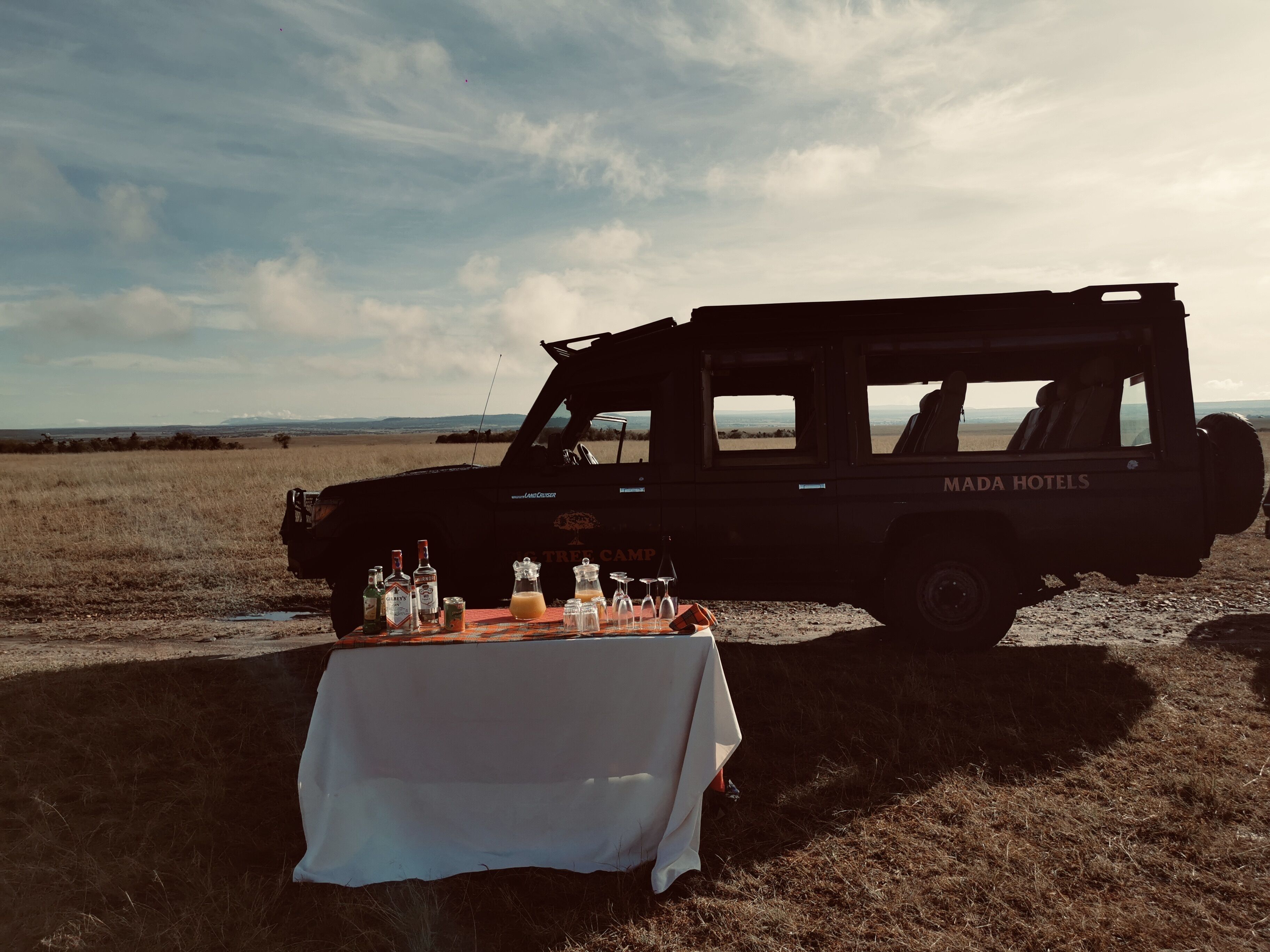 A safari vehicle with a table set up in front, featuring various bottles and glasses.
