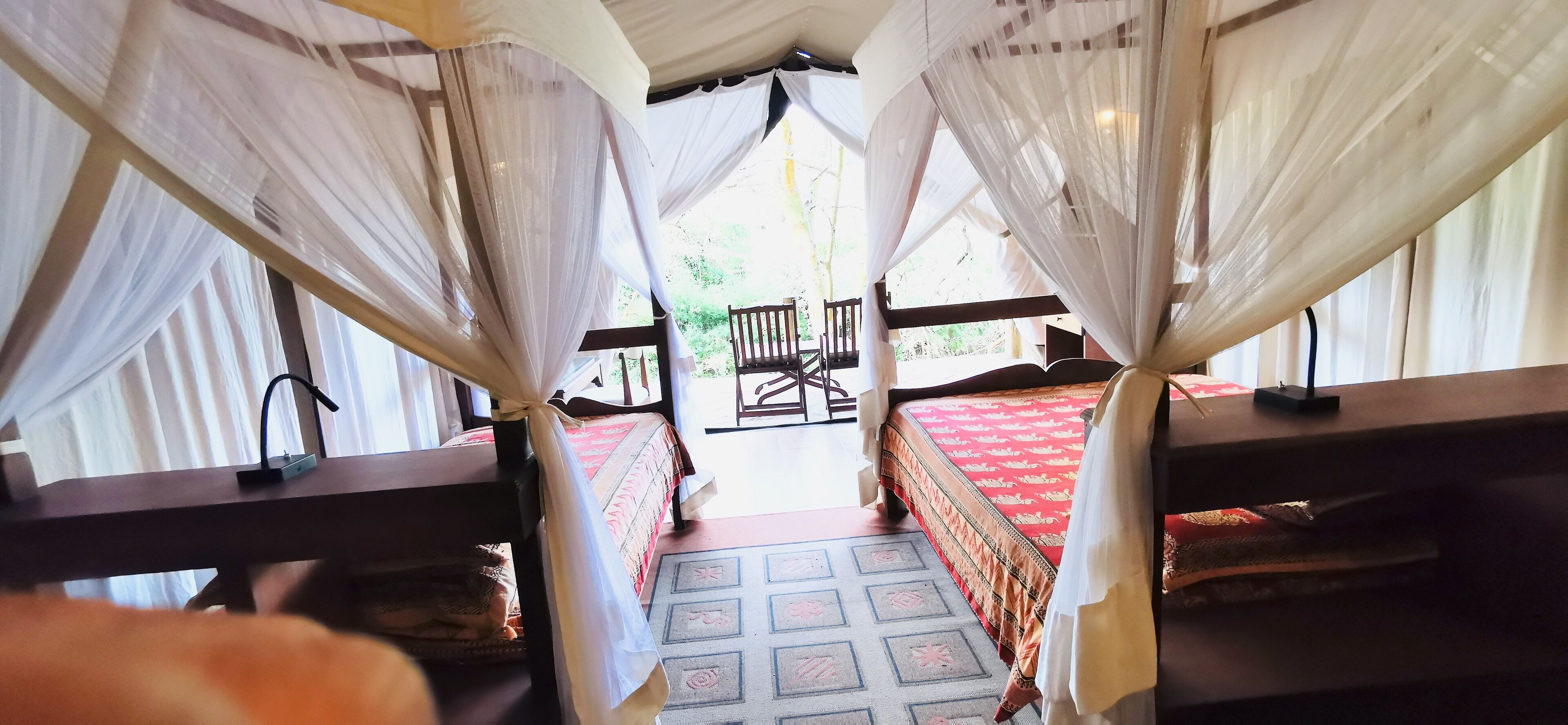 A room with two beds, each with a red bedspread, and a wooden bench. The room has a canopy bed with white curtains.
