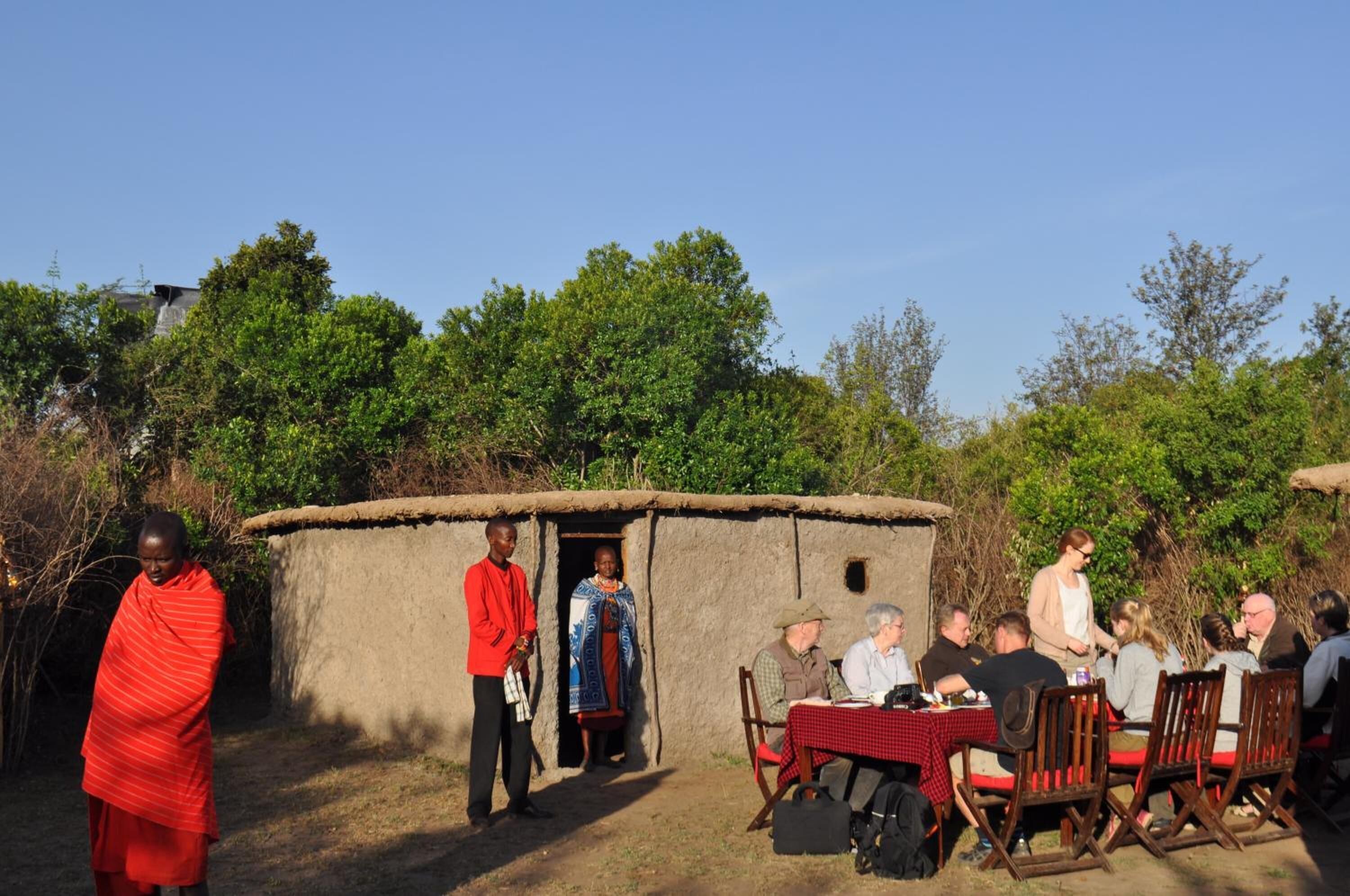 A rustic outdoor dining area with a thatched-roof hut, wooden tables, and chairs.