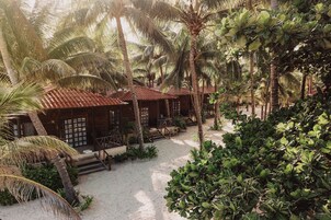 A resort with wooden cabins, palm trees, and a sandy courtyard.