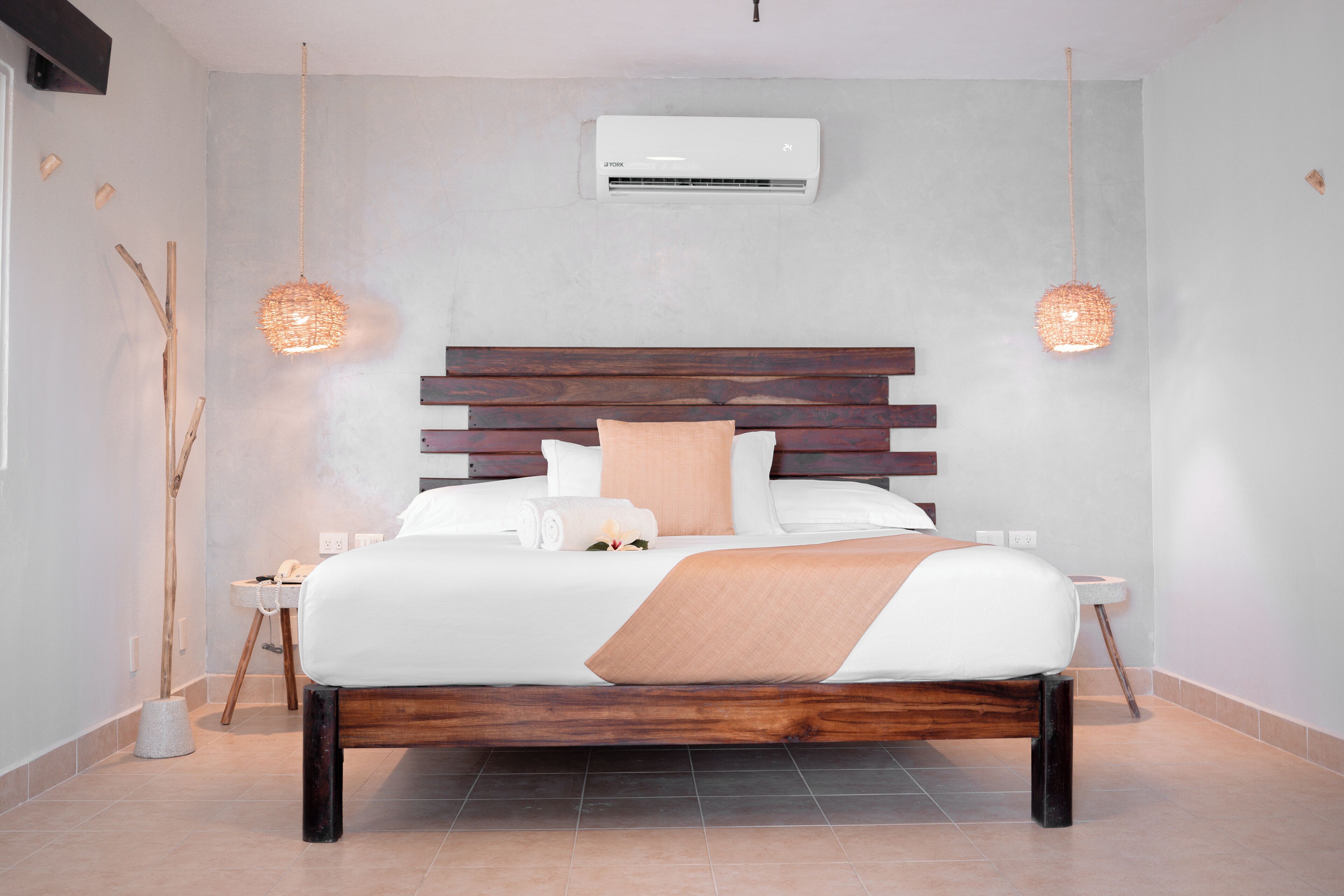 Un dormitorio moderno con cabecera de madera, ropa de cama blanca y dos lámparas colgantes.