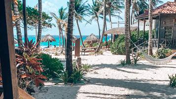 A beach view with a wooden staircase leading to a covered area, palm trees, and a clear sky.