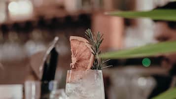 A bar setting with a tall glass containing a layered drink, garnished with a flower and a sprig of rosemary.