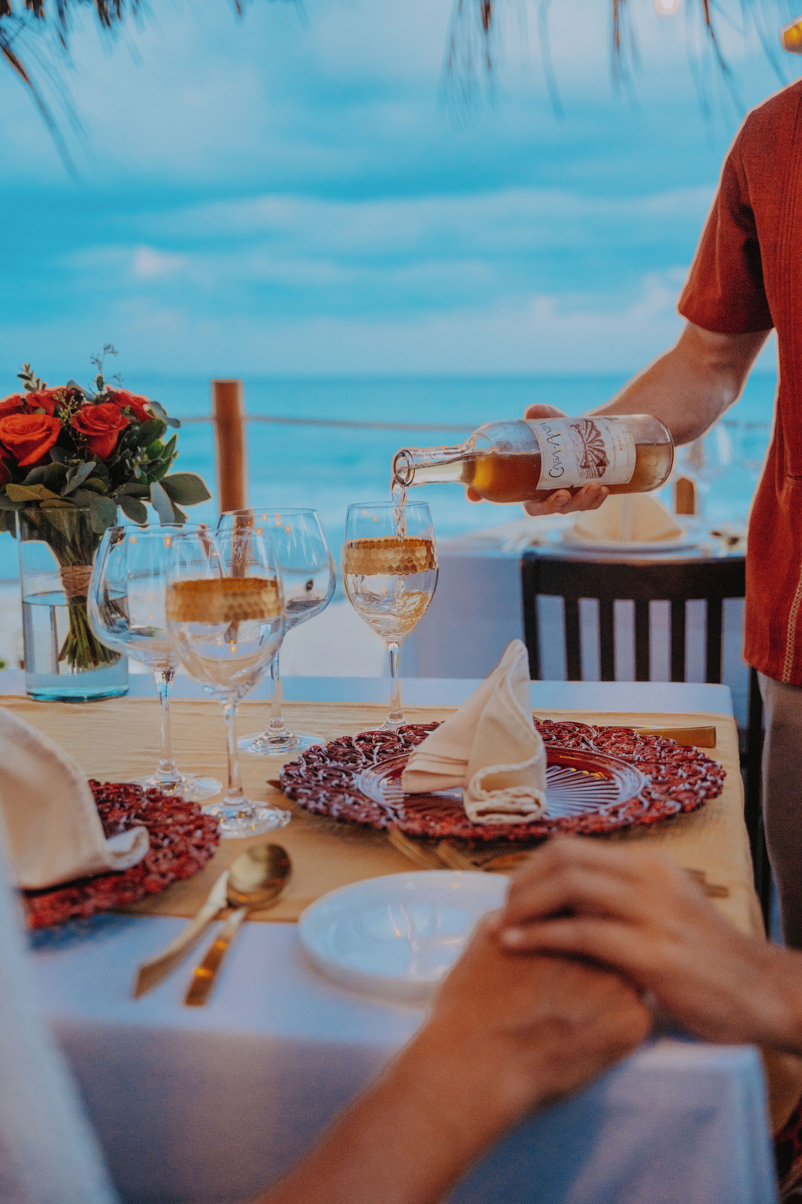 A table set for a meal with wine glasses, a bottle of wine, and a vase with red roses.