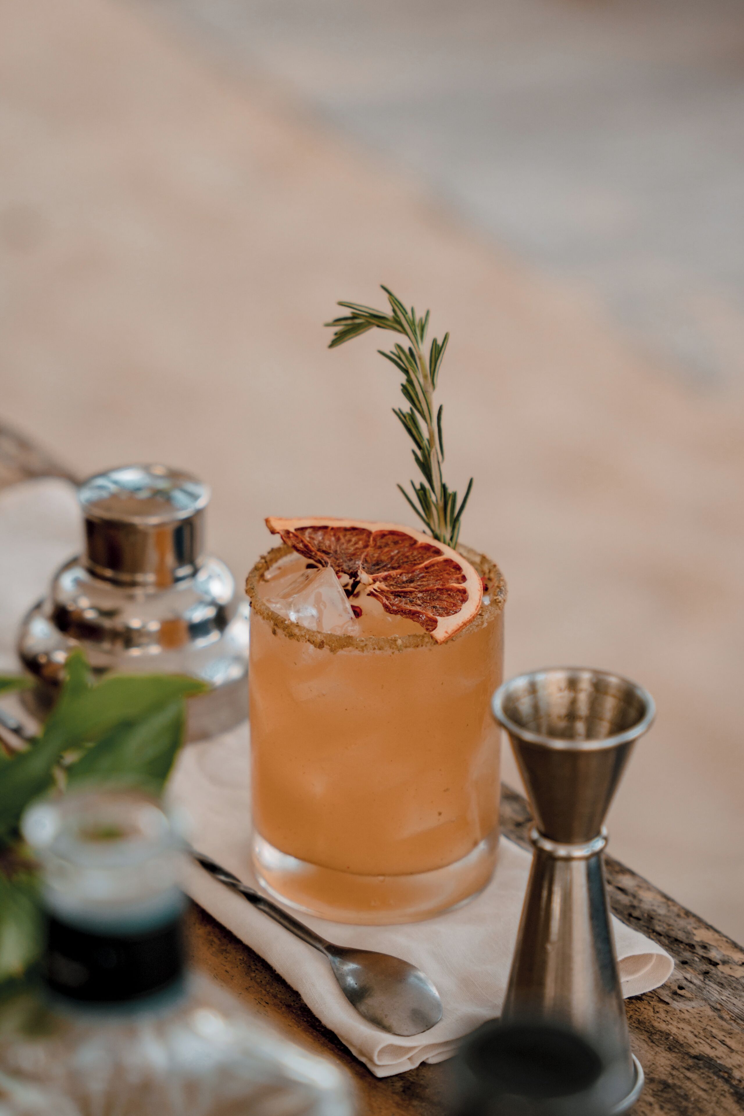 A cocktail glass with a garnish, a salt shaker, and a spoon on a wooden table.