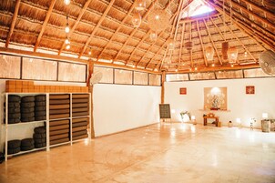 Una habitación amplia con techo de paja, un ventilador y un pequeño altar con velas.