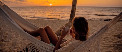 Una hamaca en una playa arenosa con un atardecer de fondo.