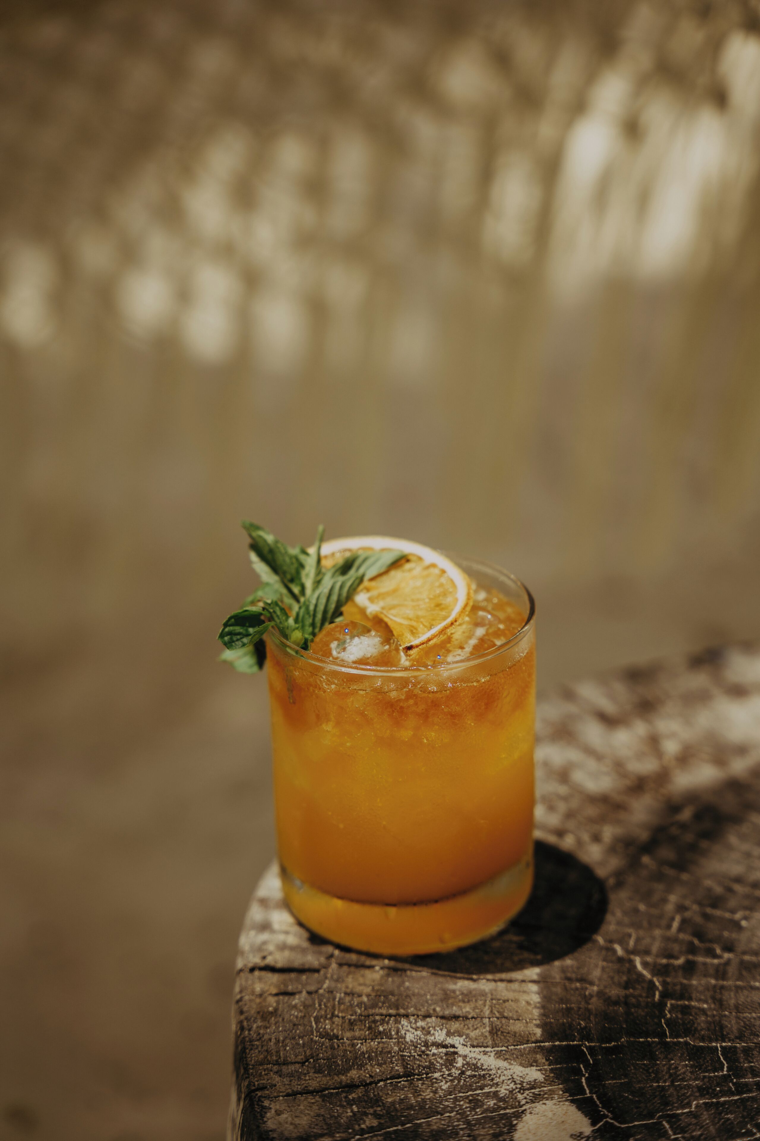 Un verre d’une boisson ambrée, agrémenté d’une tranche d’orange et d’une feuille de menthe, posé sur une surface en bois.