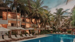 A hotel pool area with lounge chairs and umbrellas, surrounded by palm trees and a multi-story building with balconies. - Petit Lafitte Beachfront Hotel & Bungalows (Playa del Carmen)