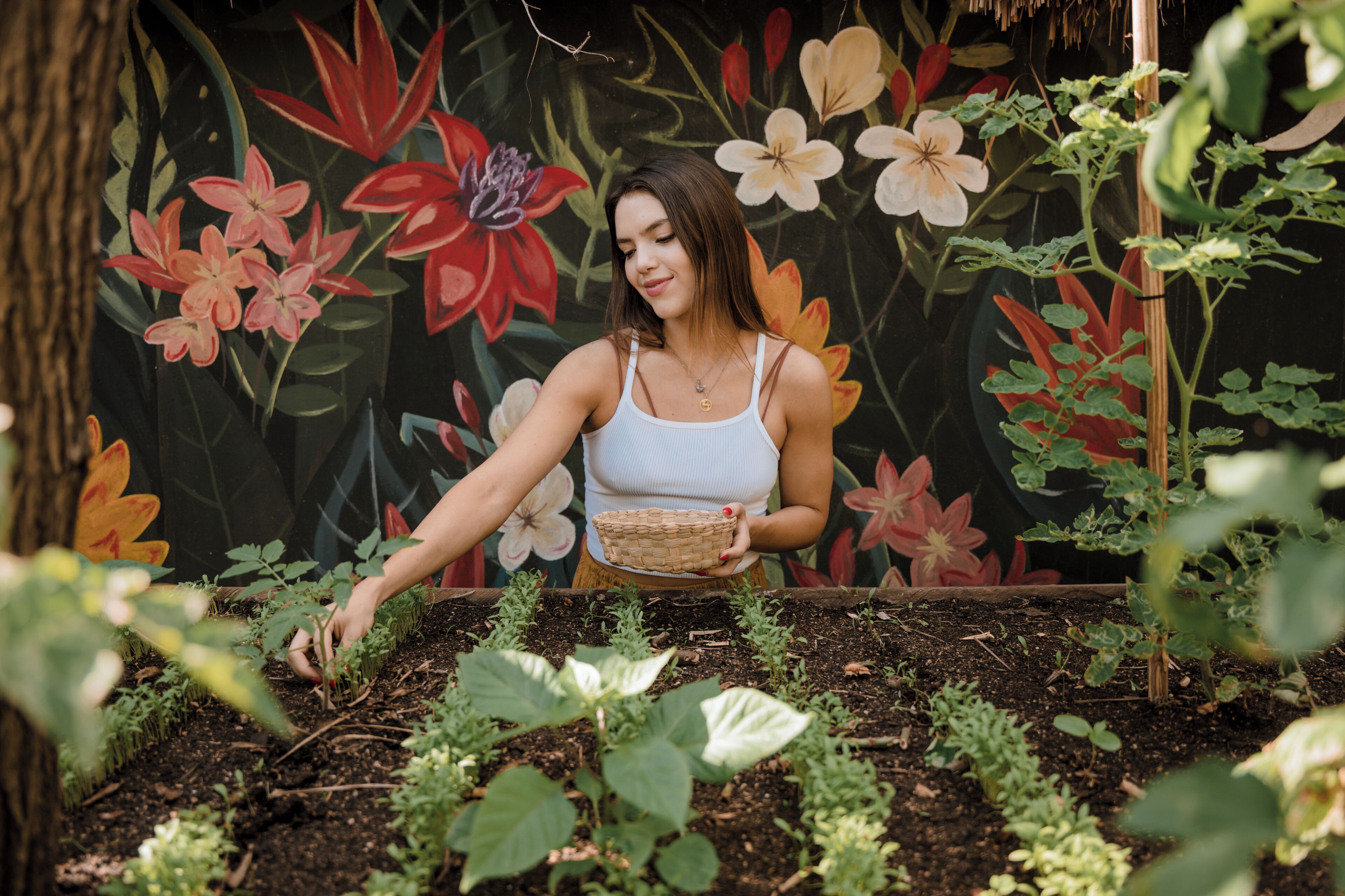 A person tending to a garden with a variety of plants and a mural of flowers in the background.