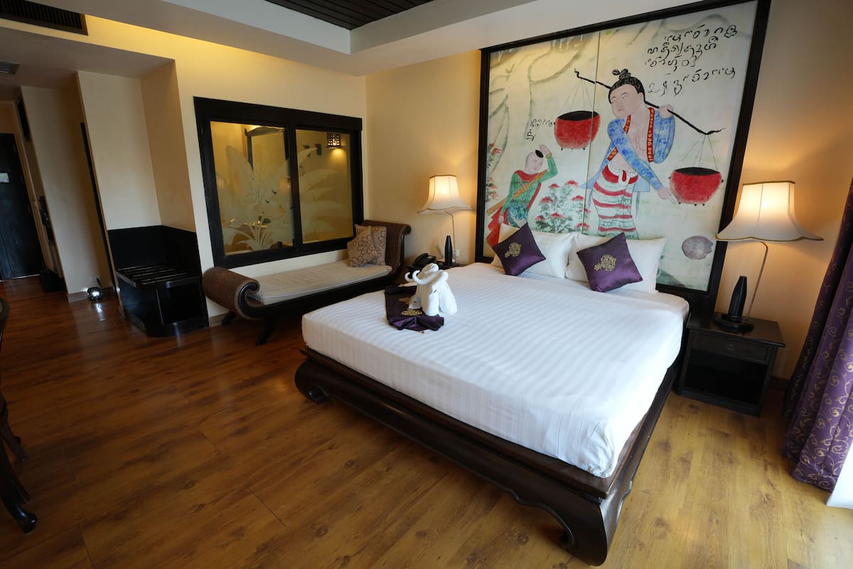 A hotel room with two beds, wooden flooring, a large painting on the wall, and two bedside lamps.
